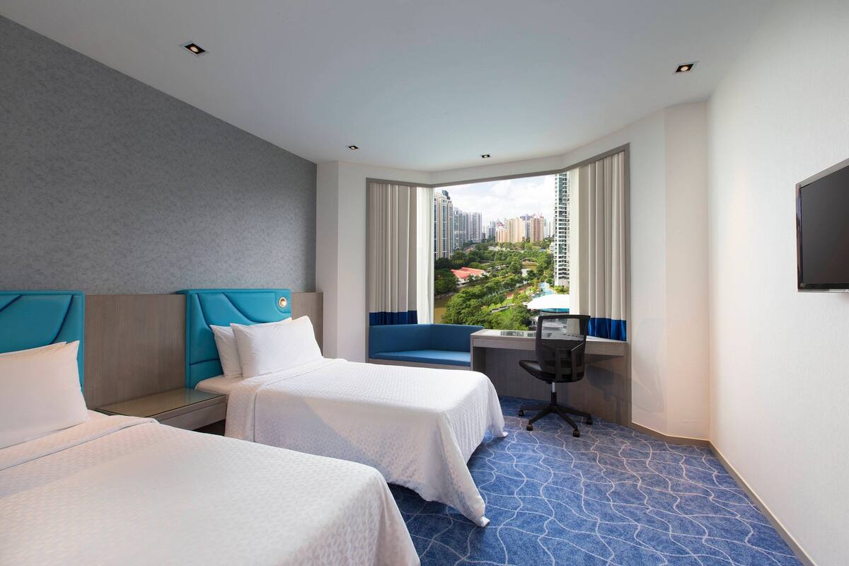 Une chambre d’hôtel avec deux lits, un bureau et une grande fenêtre donnant sur la ville.