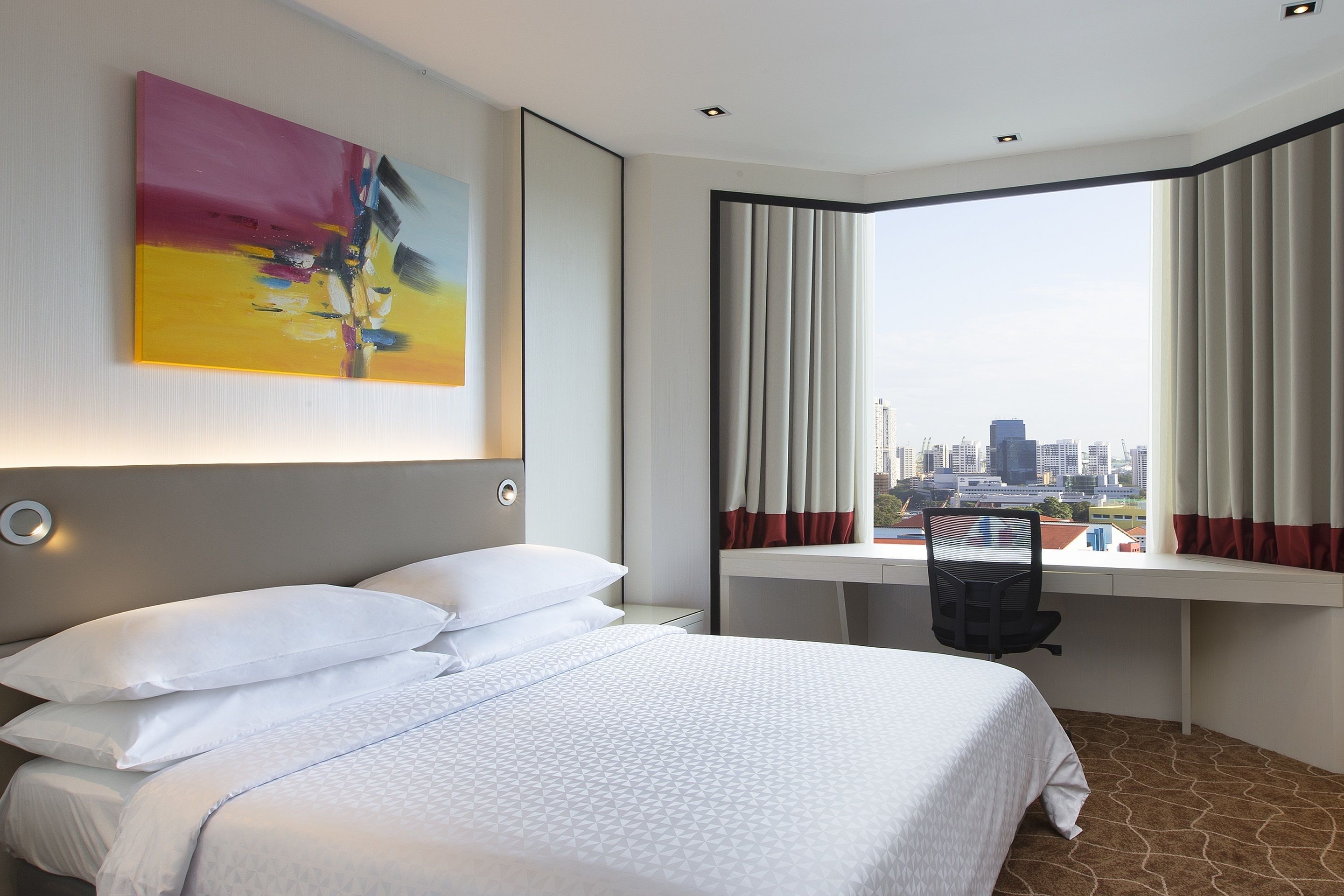 Ein Hotelzimmer mit einem Bett, einem Schreibtisch und einem großen Fenster mit Vorhängen.