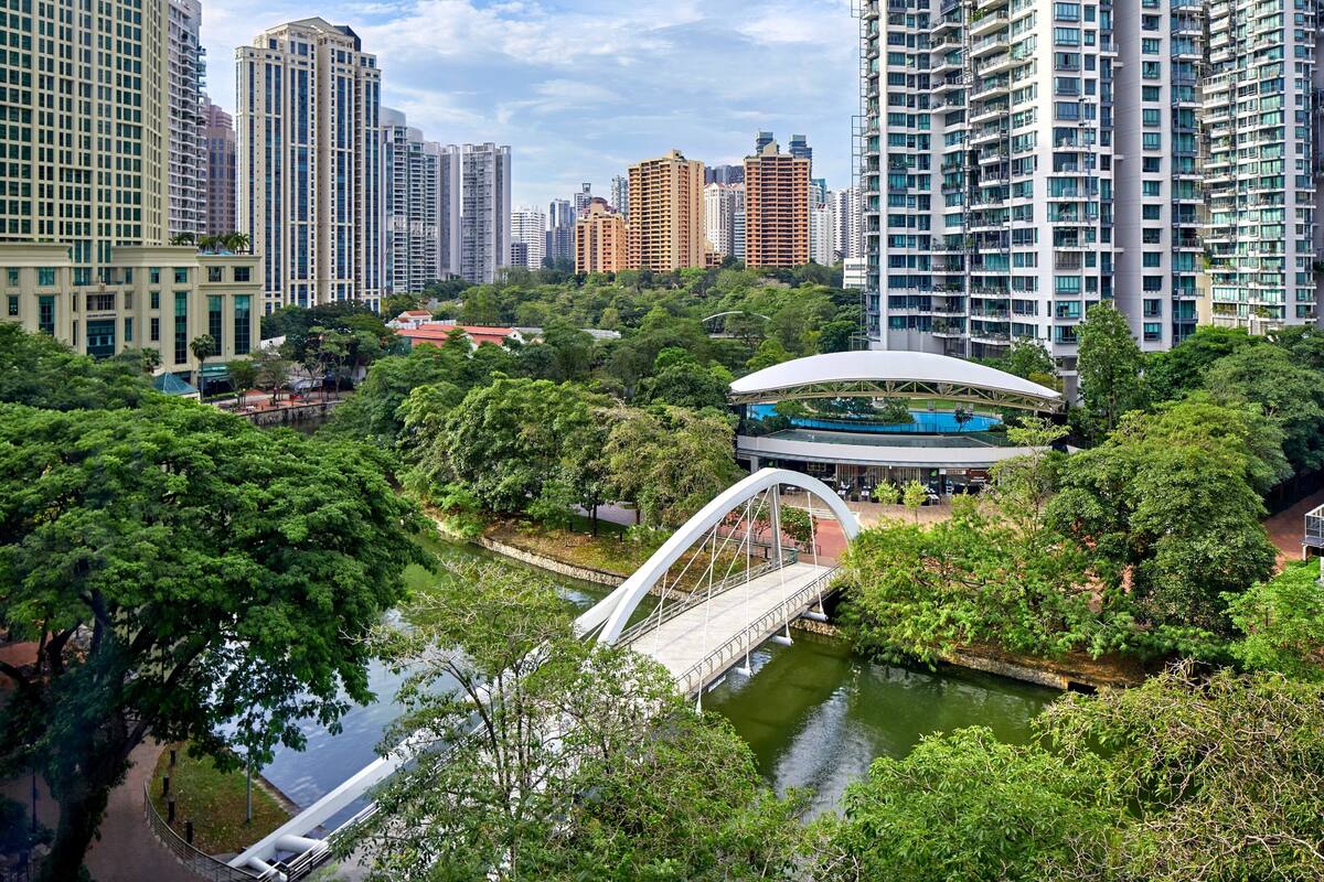 Un parc urbain moderne avec un pont, un lac et des immeubles de grande hauteur en arrière-plan.