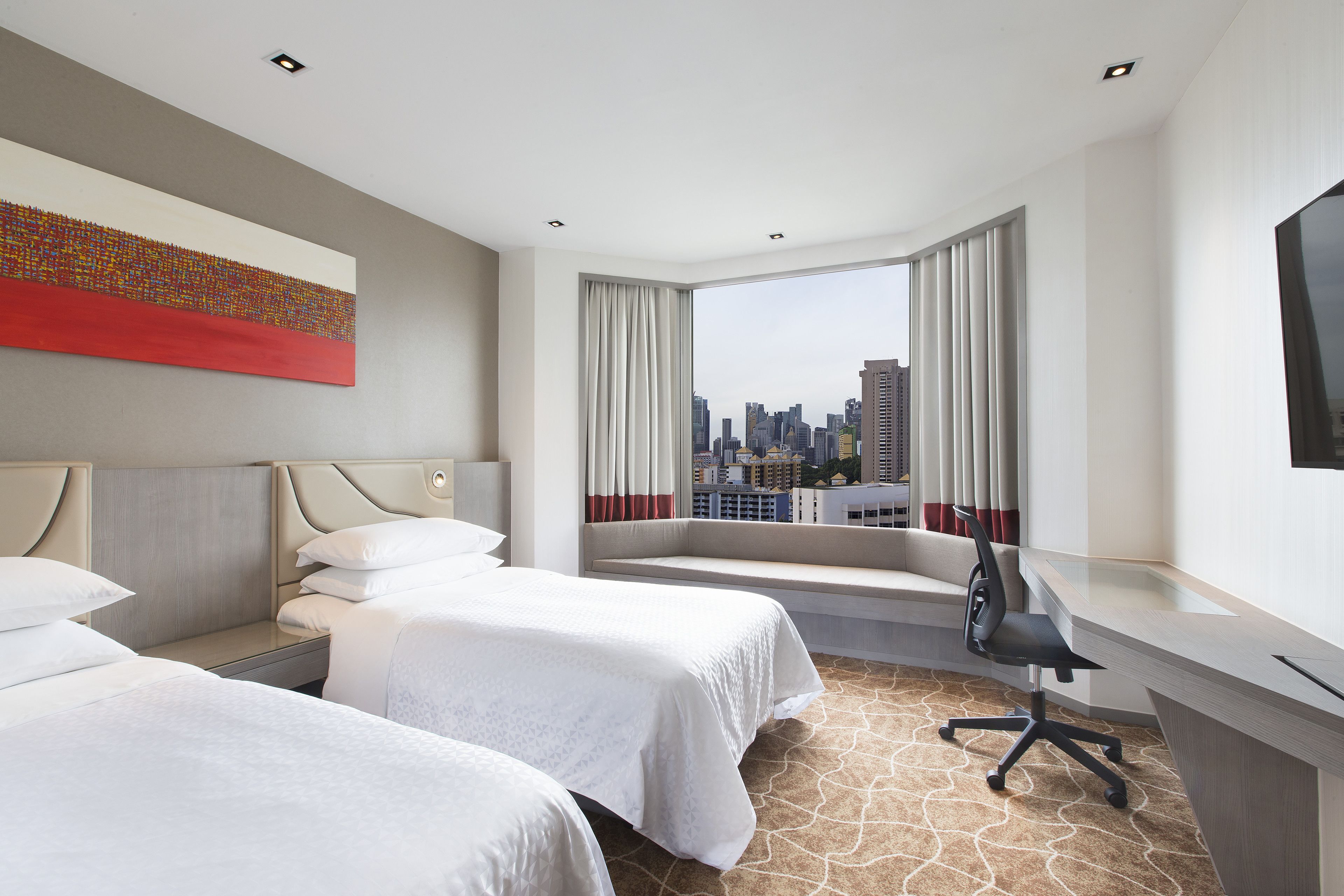 A hotel room with two beds, a desk, and a large window with a city view.