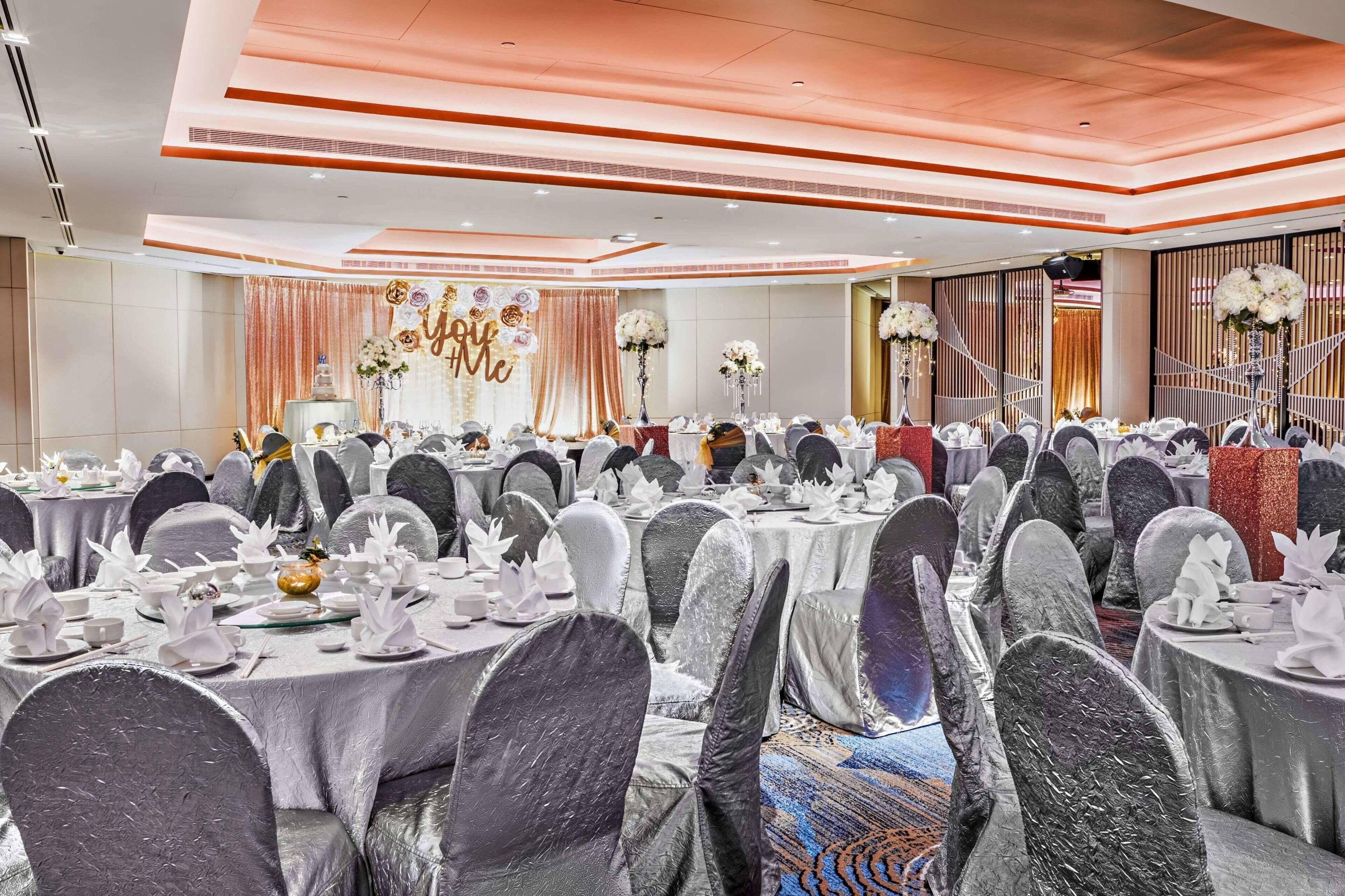 Une salle de banquet avec des tables rondes recouvertes de nappes blanches et des chaises habillées de housses grises.
