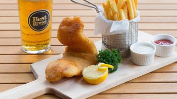 A meal of fish and chips, a glass of beer, and two small dipping sauces on a wooden table.