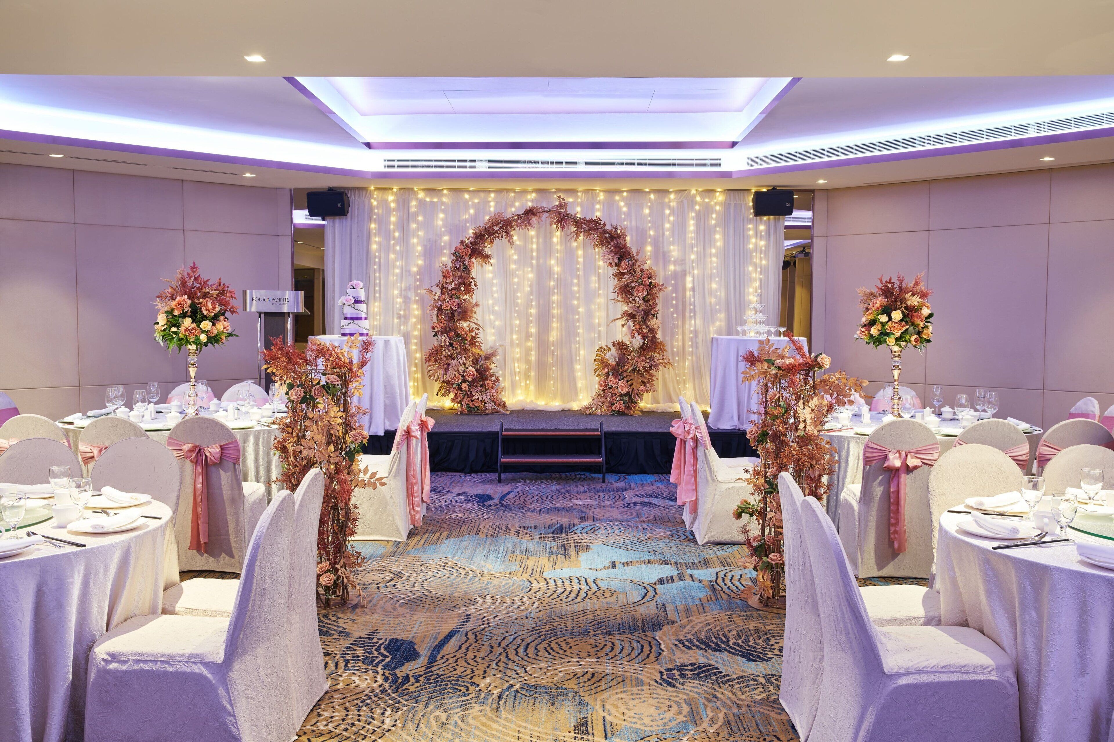 Une salle de banquet avec des tables rondes, des chaises blanches et des centres de table ornés de compositions florales.