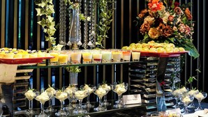 Una mesa de buffet con diversos alimentos y bebidas, decorada con arreglos florales y follaje.