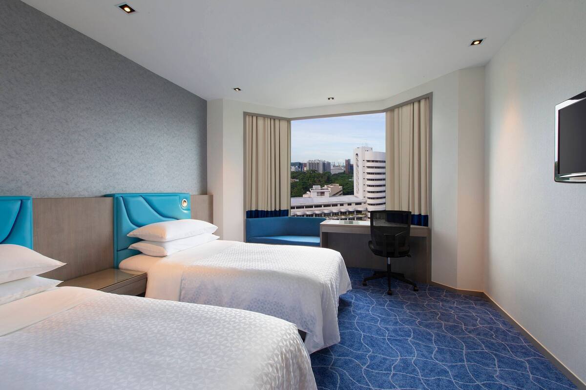Une chambre d’hôtel avec deux lits, un bureau et une vue sur les immeubles.