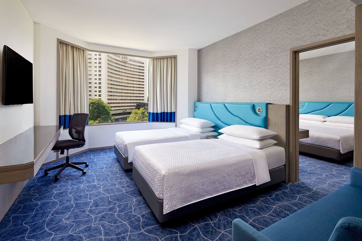 Une chambre d’hôtel avec deux lits, un bureau, une chaise, une télévision et une grande fenêtre avec des rideaux.