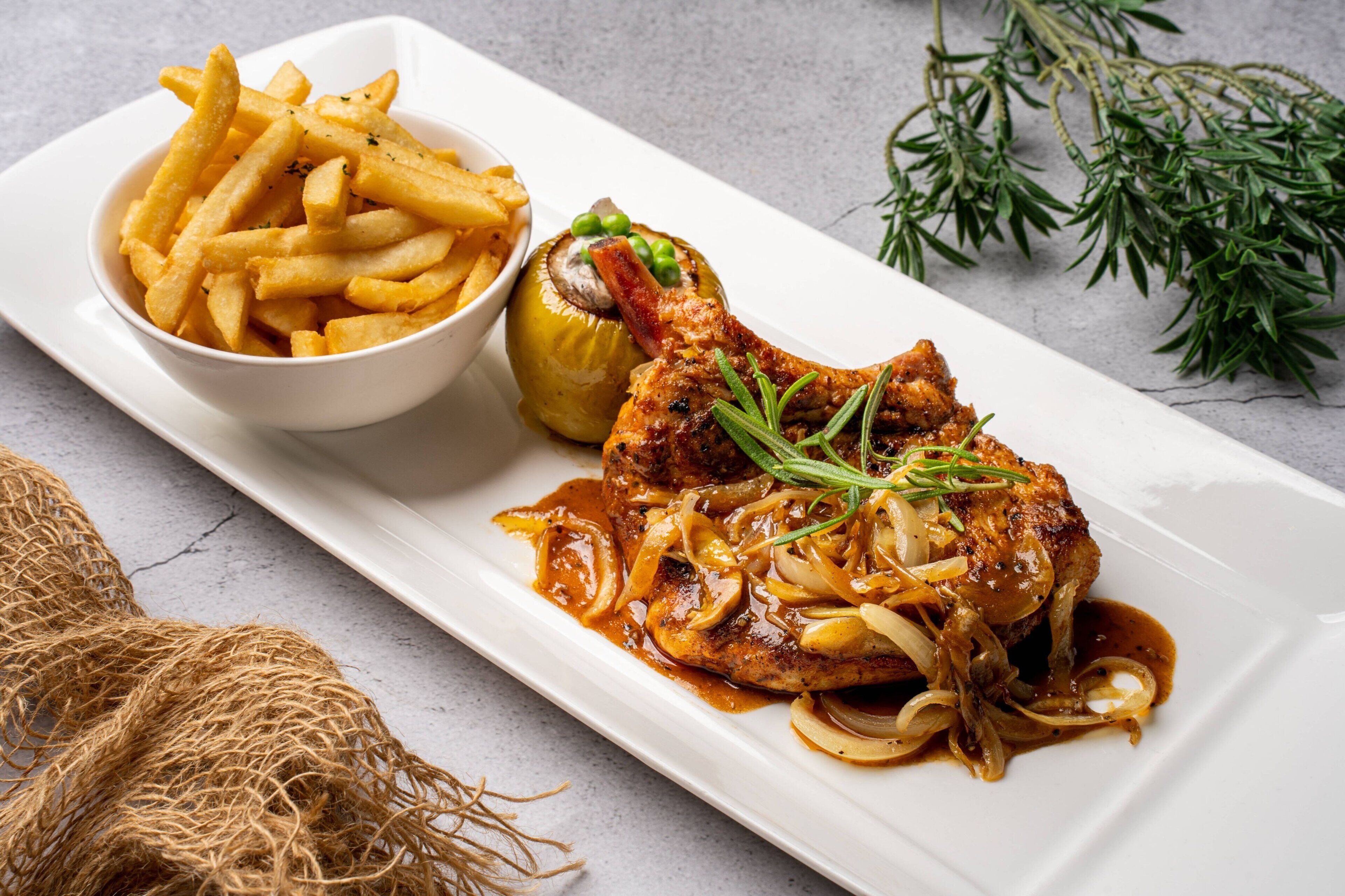 Une assiette comprenant un morceau de poulet grillé, des champignons et des oignons, accompagnée d’un bol de frites et d’un légume farci.