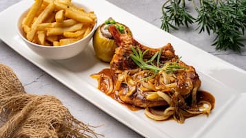 Une assiette comprenant un morceau de poulet grillé, des champignons et des oignons, accompagnée d’un bol de frites et d’un légume farci.