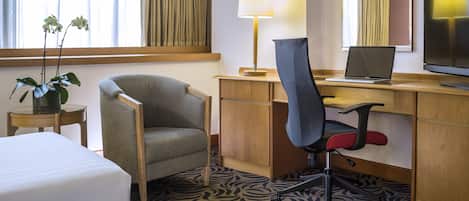 Habitación de hotel con cama, escritorio, computadora portátil, silla, lámpara y televisor.
