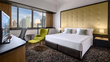Ein Hotelzimmer mit einem großen Bett, einem Schreibtisch mit Stuhl, einem kleinen Tisch und Blick auf die Stadt durch große Fenster.