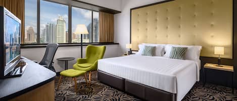 Habitación de hotel con una cama grande, un escritorio con silla, una mesita y vistas a la ciudad a través de amplios ventanales.