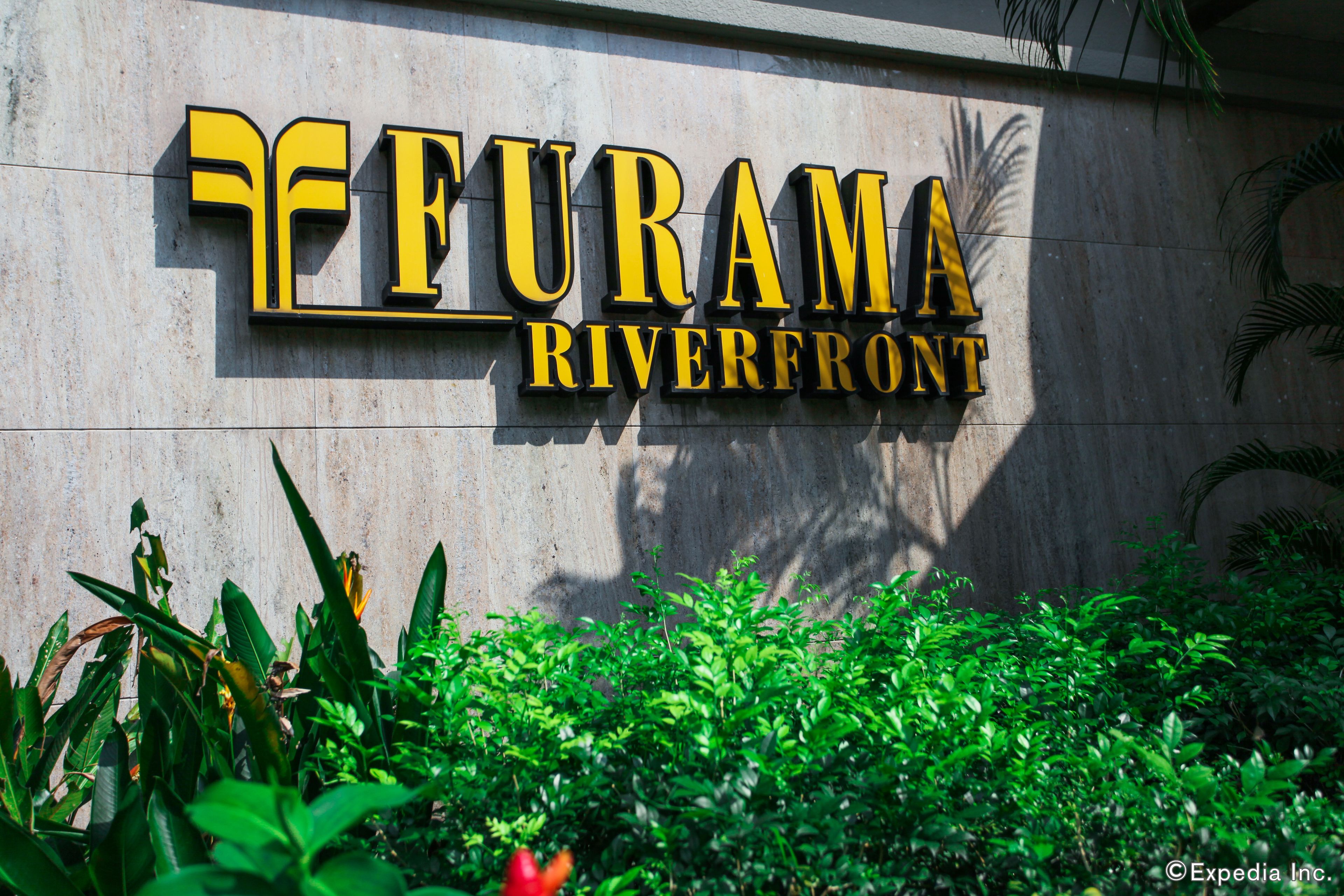 A sign for 'Furama Riverfront' with a modern design and greenery in front.
