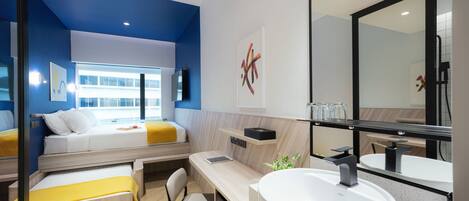 A modern hotel room with a bed, desk, chair, and a large bathroom mirror.