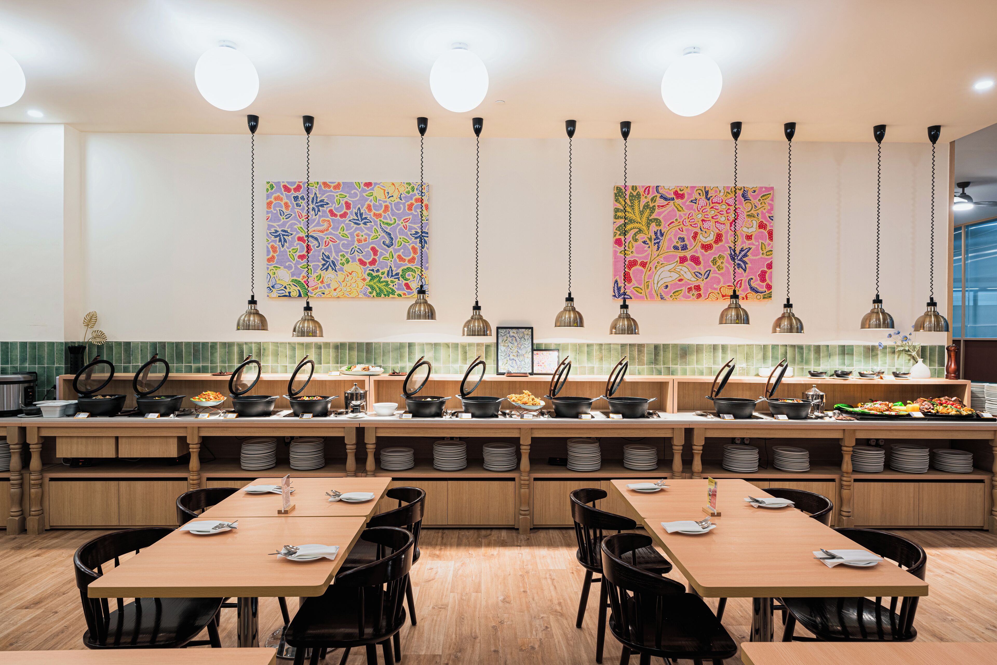 A modern kitchen with multiple cooking stations, hanging pendant lights, and colorful artwork on the walls.