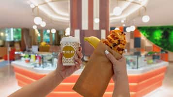 A person holding a coffee cup and a wrapped food item in a brightly lit indoor setting with a modern design.