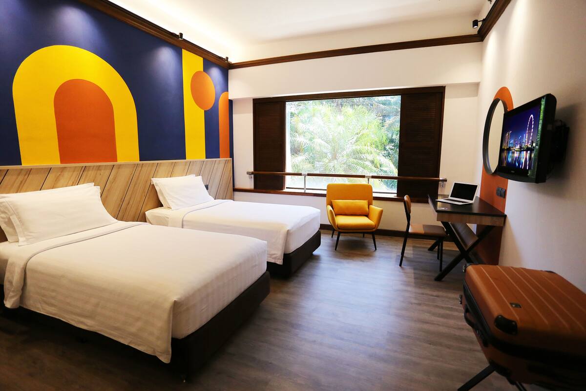 A hotel room with two beds, a desk, a chair, a TV, and a suitcase.