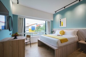 A modern hotel room with a bed, bedside table, and a view of buildings outside.