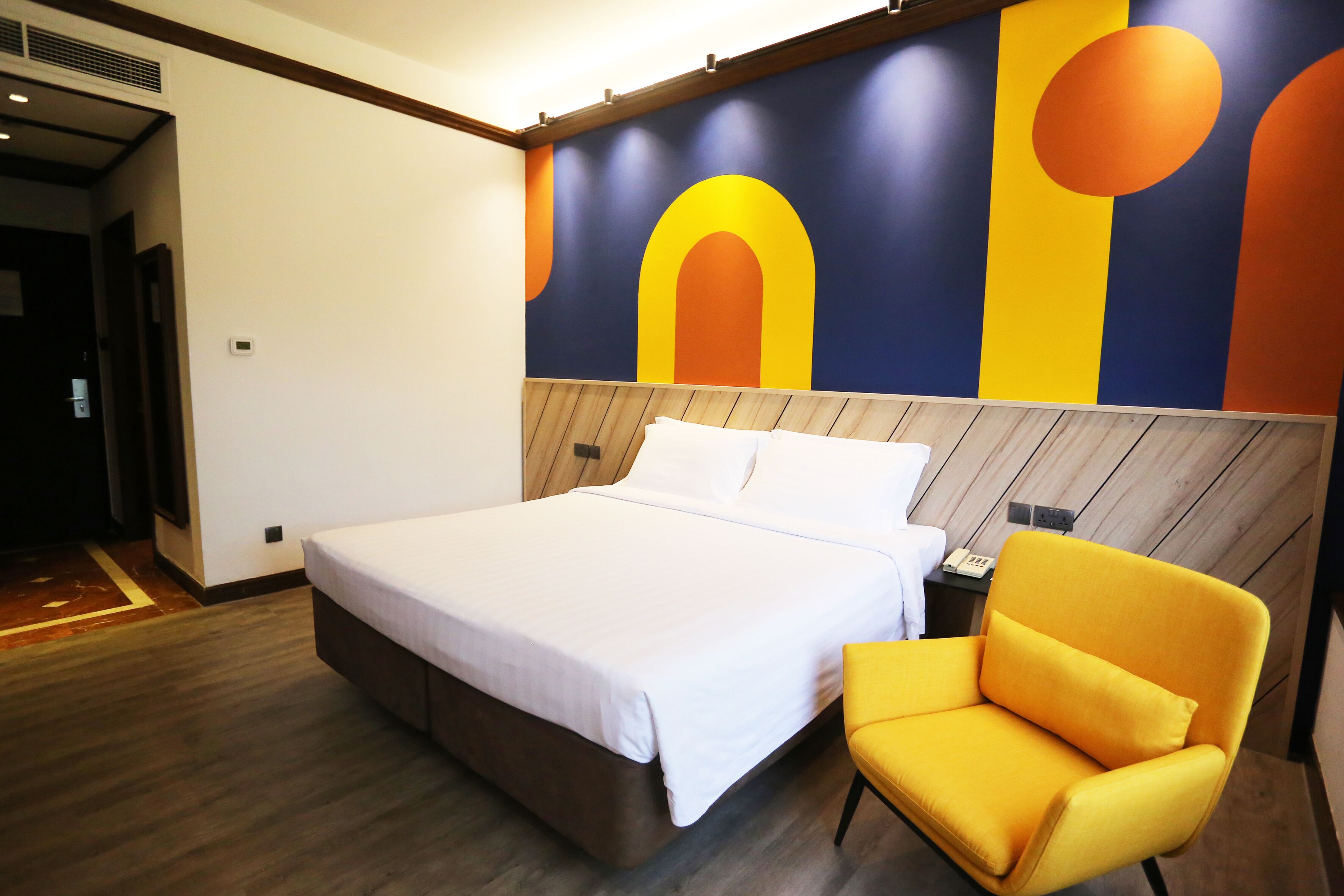 A modern hotel room with a large bed, a wooden headboard, and a vibrant abstract mural on the wall.