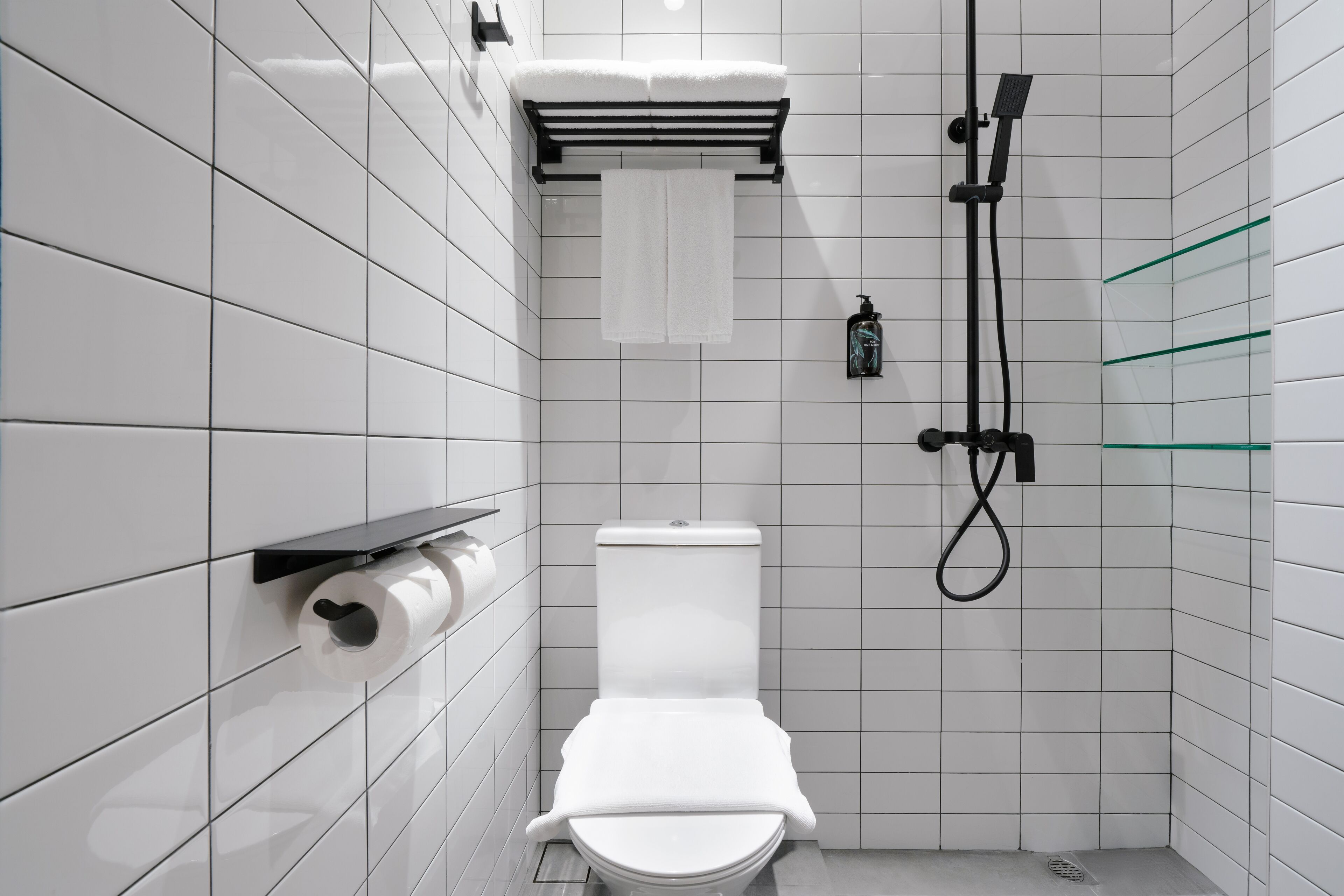 Een moderne badkamer met witte tegels, toilet, douche en een glazen plank.