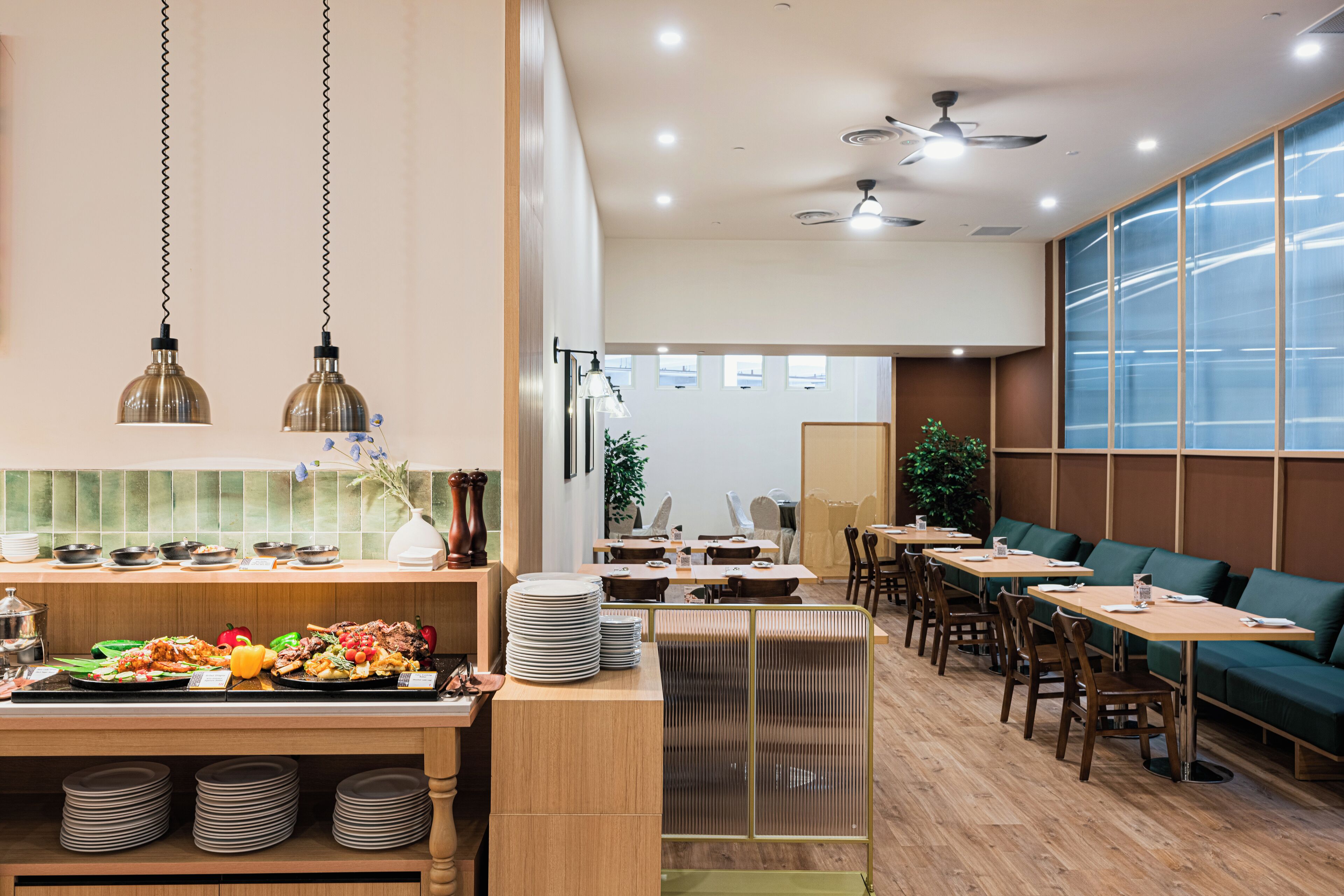 A restaurant with a buffet area, multiple tables, and a seating area with green upholstered benches.