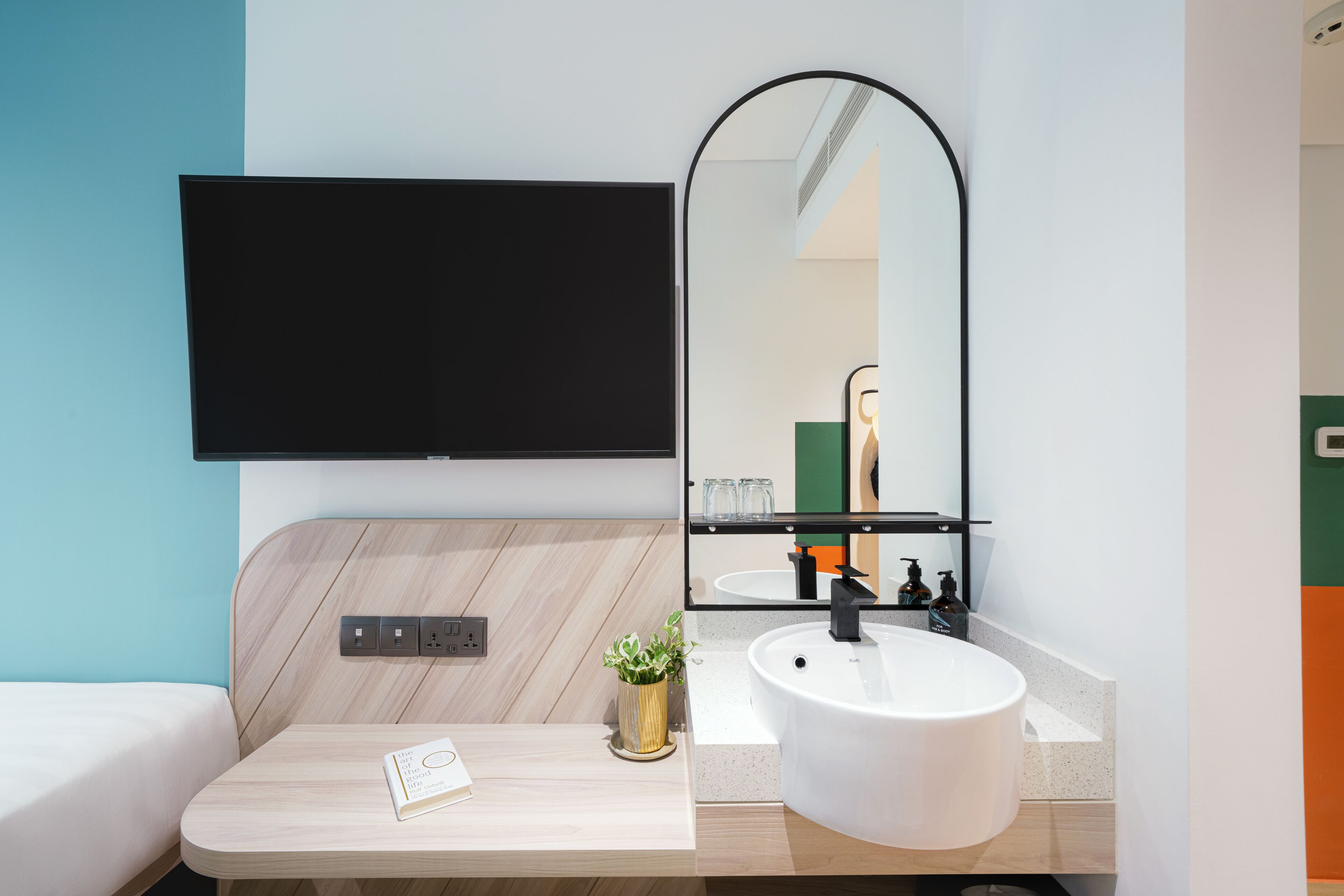 Une salle de bain moderne équipée d’un téléviseur mural, d’un lavabo et d’un miroir.
