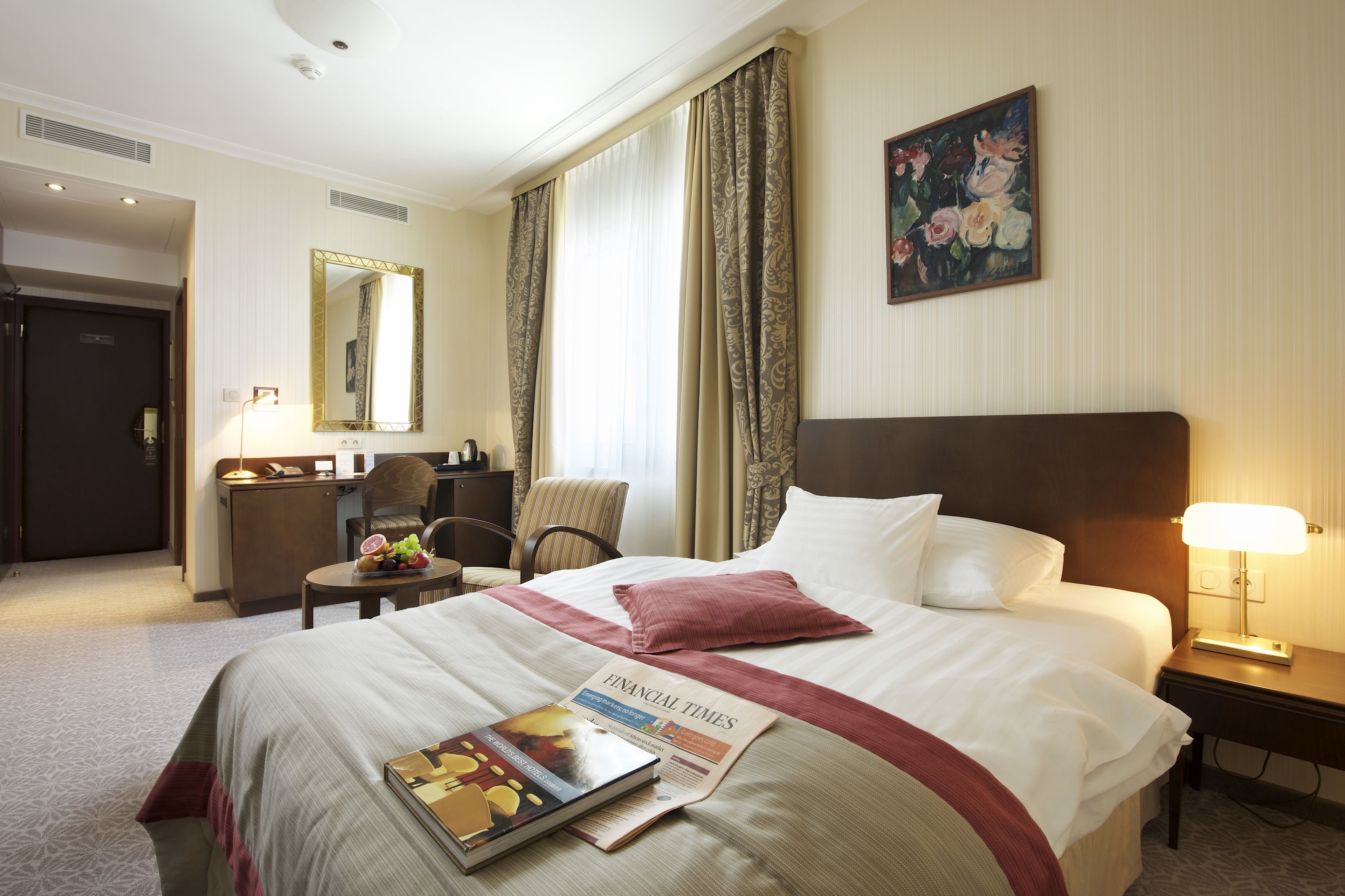 A hotel room with a large bed, a desk with a chair, a mirror, and a painting on the wall.