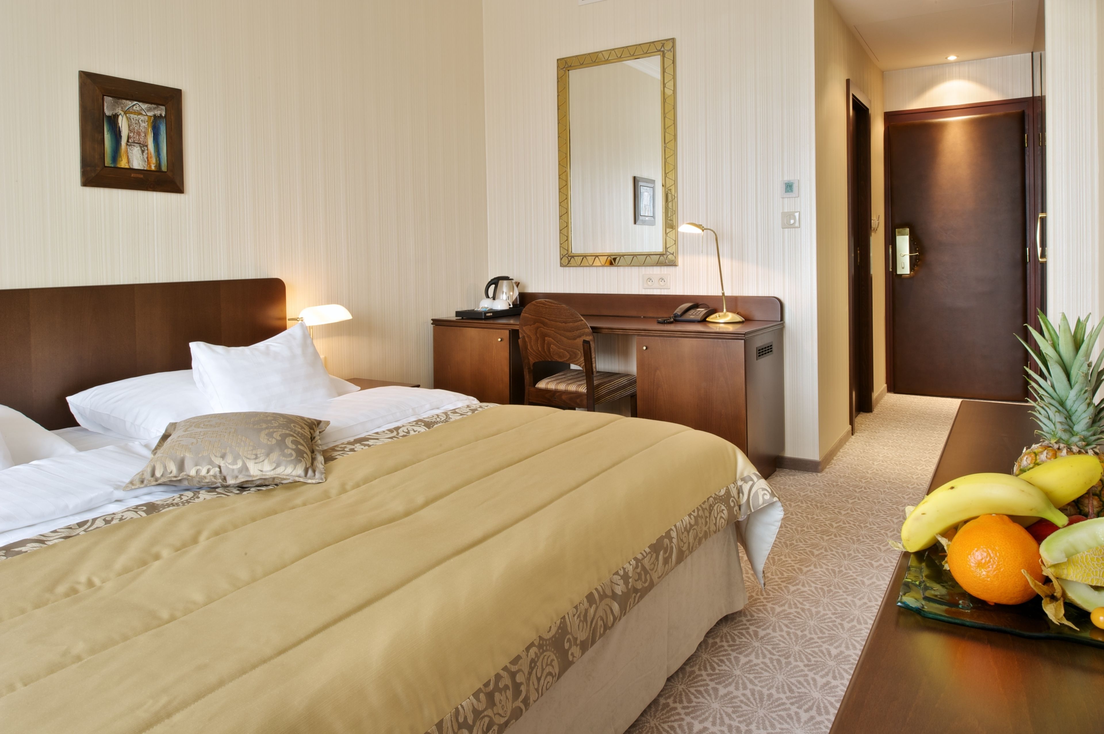 A hotel room with a bed, desk, chair, and a fruit tray on the side.