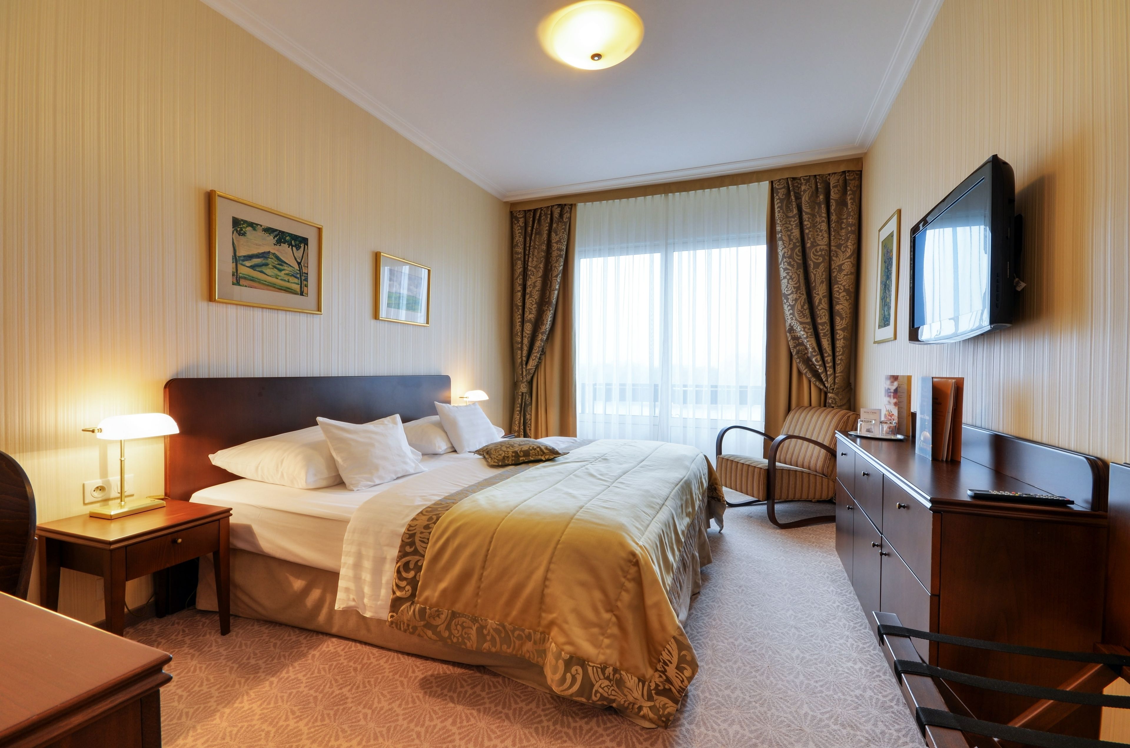 Ein Hotelzimmer mit einem großen Bett, einem Schreibtisch mit Lampe, einem Fernseher und einem Sessel.