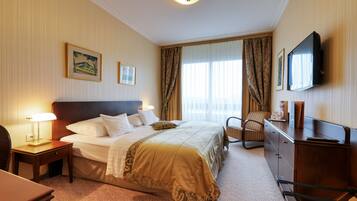 Ein Hotelzimmer mit einem großen Bett, einem Schreibtisch mit Lampe, einem Fernseher und einem Sessel.