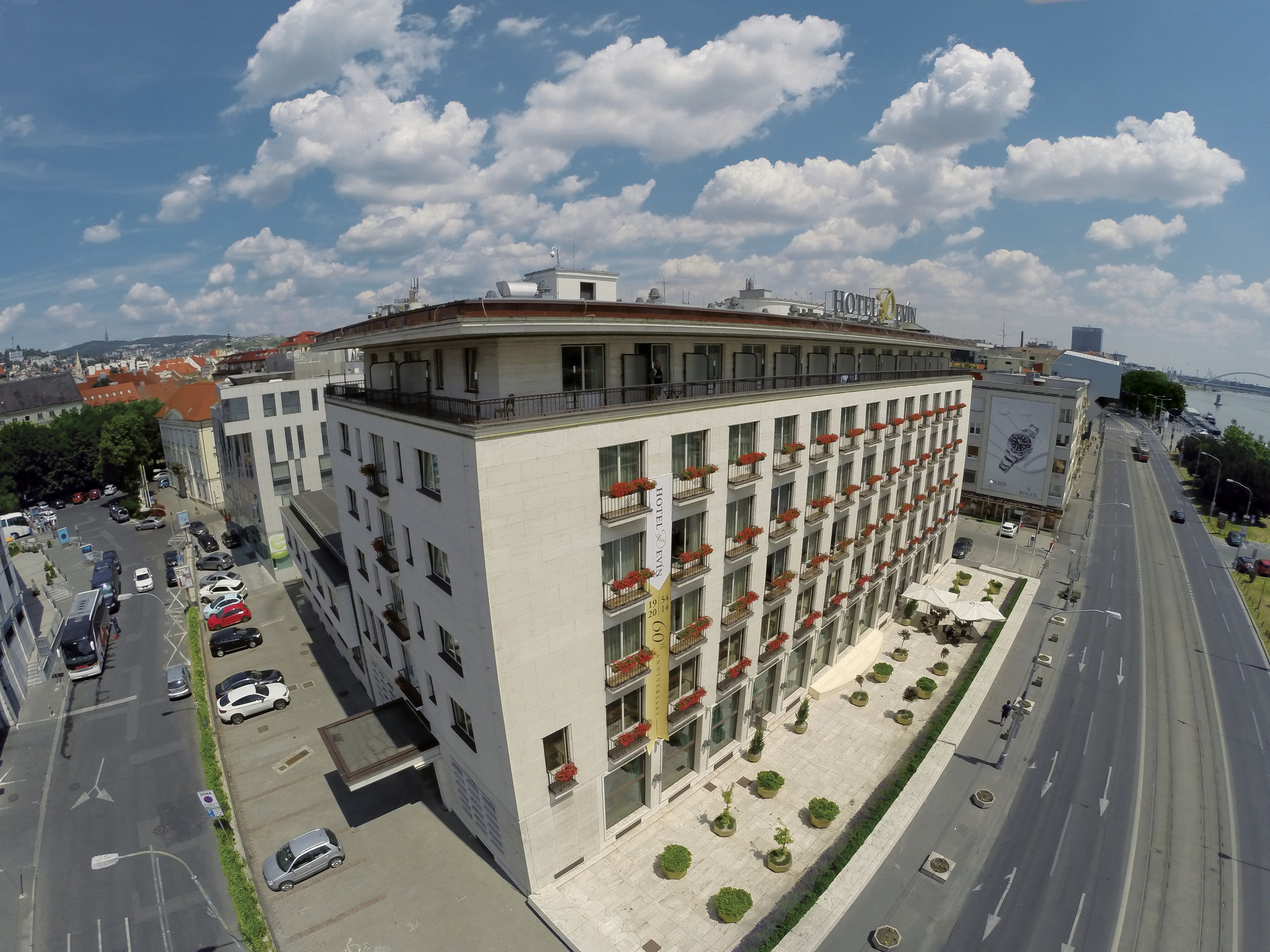 A hotel with multiple floors, balconies with red flowers, and a parking area with cars.