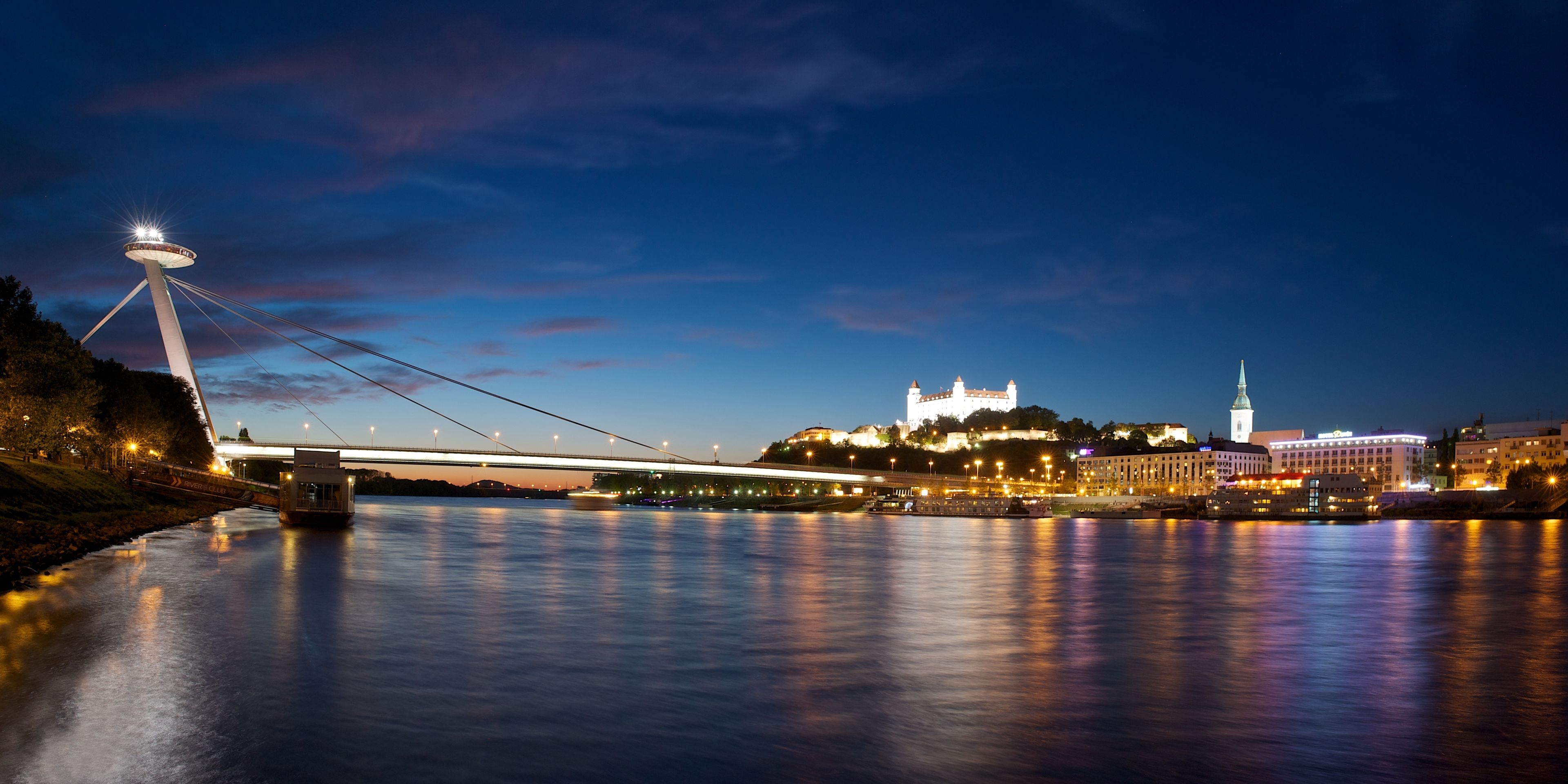 A nighttime view of a cityscape with a prominent bridge and a castle-like building with a tower.