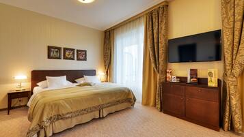 Une chambre d’hôtel avec un grand lit, un téléviseur à écran plat fixé au mur, une commode en bois et une table de chevet avec une lampe.