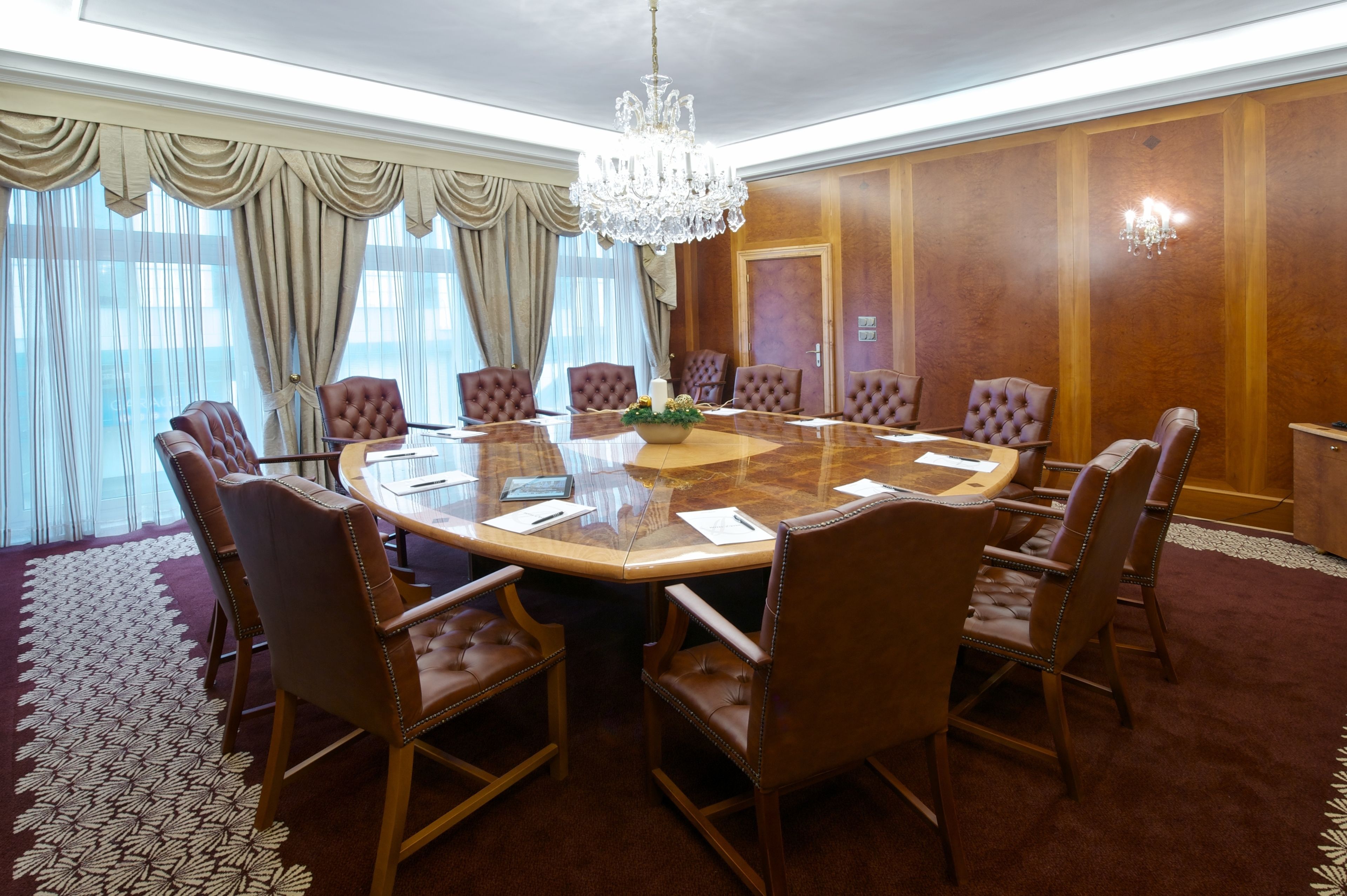 Une salle de conférence dotée d’une table ronde, de fauteuils en cuir, d’un lustre et offrant une vue sur l’extérieur grâce à de grandes fenêtres.