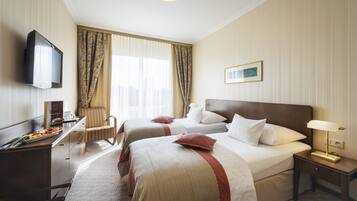 A hotel room with two beds, a desk with a TV, a chair, and a bedside table with a lamp.