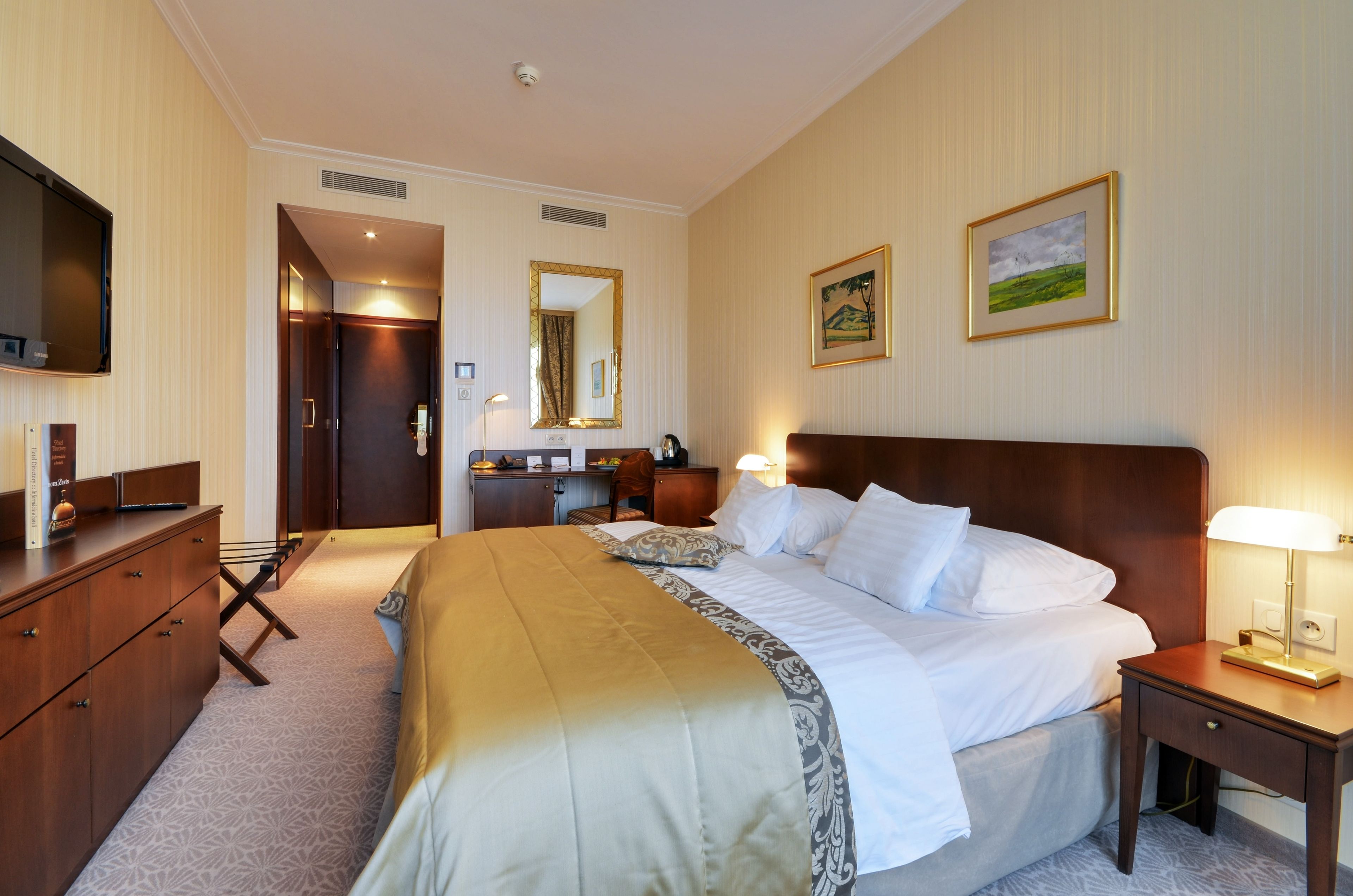 A hotel room with a bed, bedside table, desk, chair, and a television.