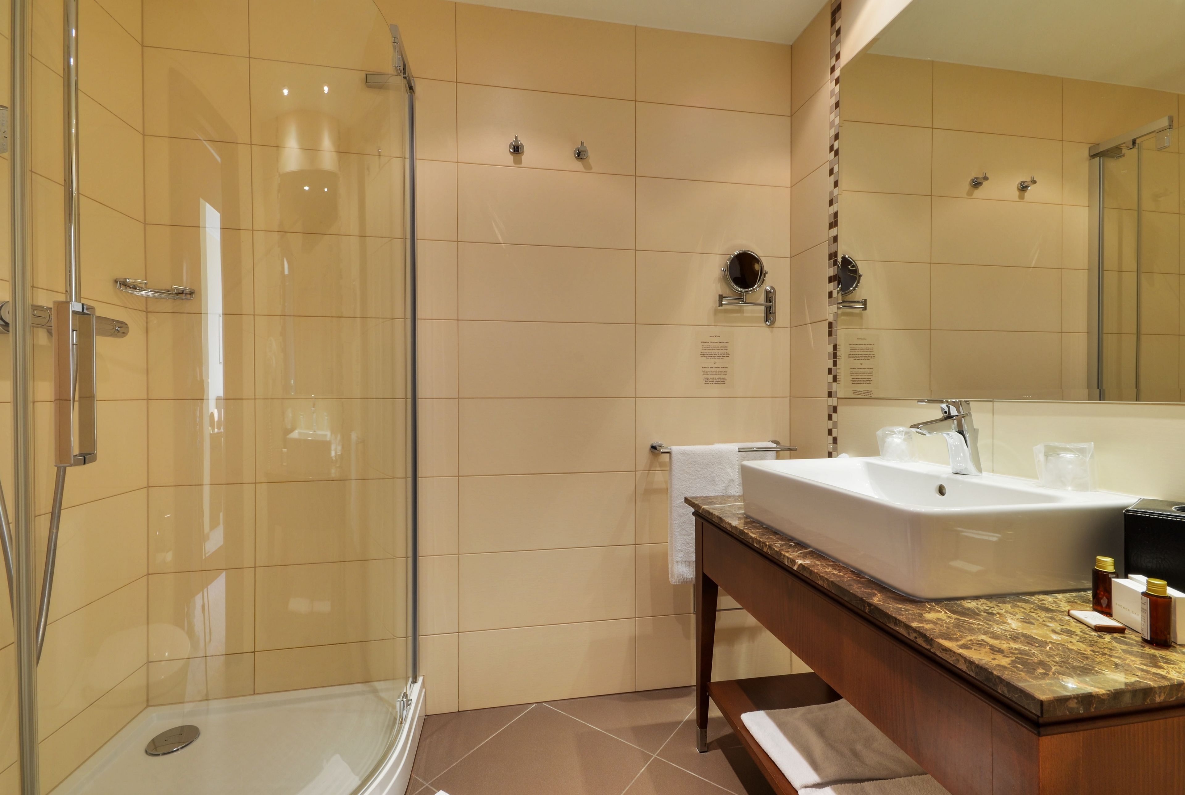 A modern bathroom with a glass-enclosed shower, a large sink with a marble countertop, and a mirror above the sink.