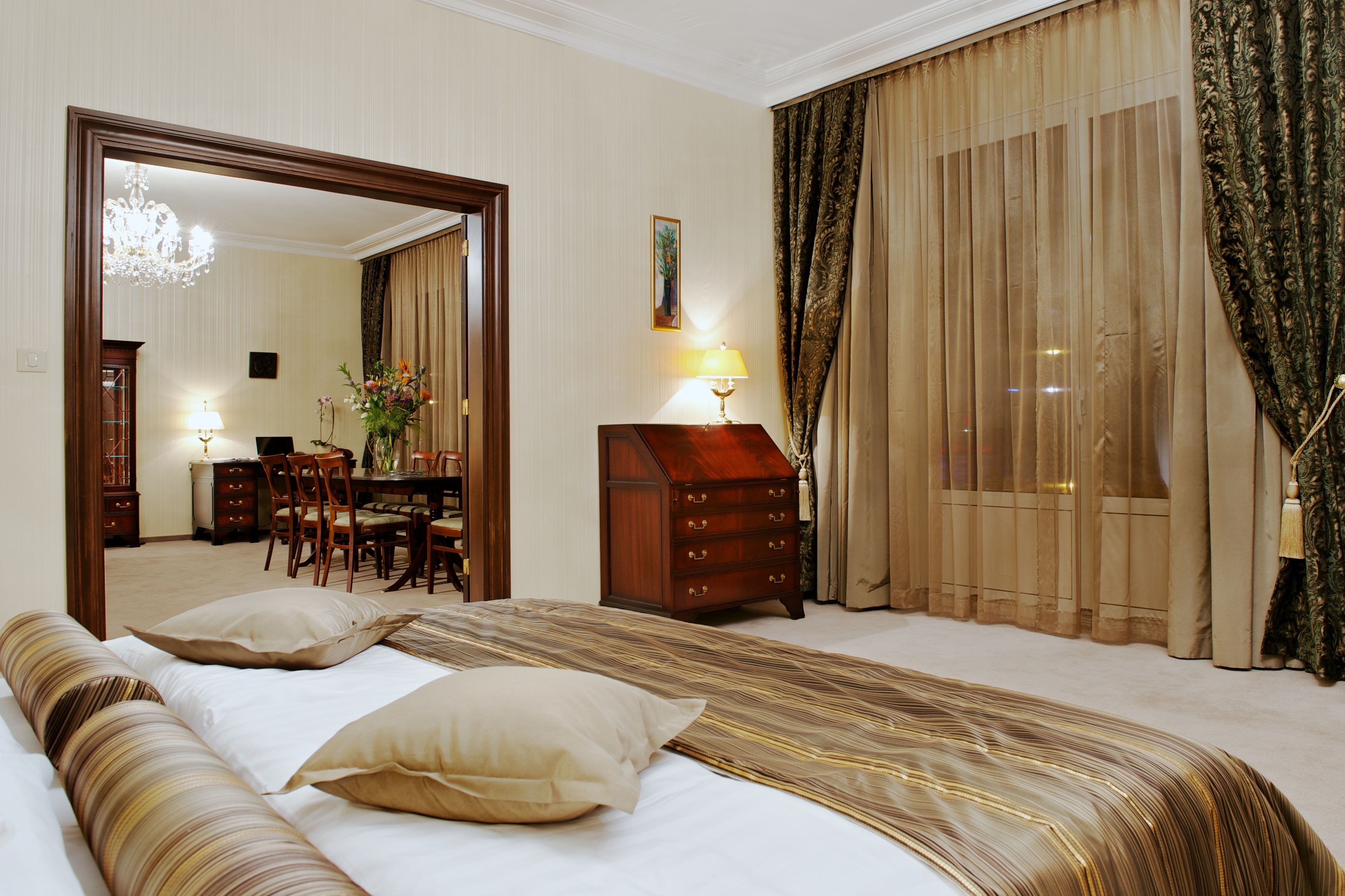 A hotel room with a large bed, a wooden dresser, a desk with chairs, and a large mirror.