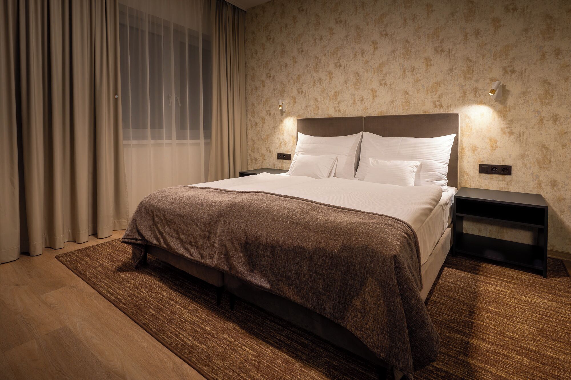 A neatly made bed with a headboard, a bedside table, and a wall-mounted light fixture.