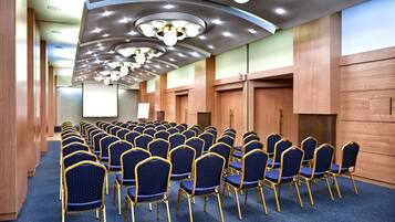 A conference room with rows of blue chairs and gold frames, wooden paneling, and modern ceiling lights.