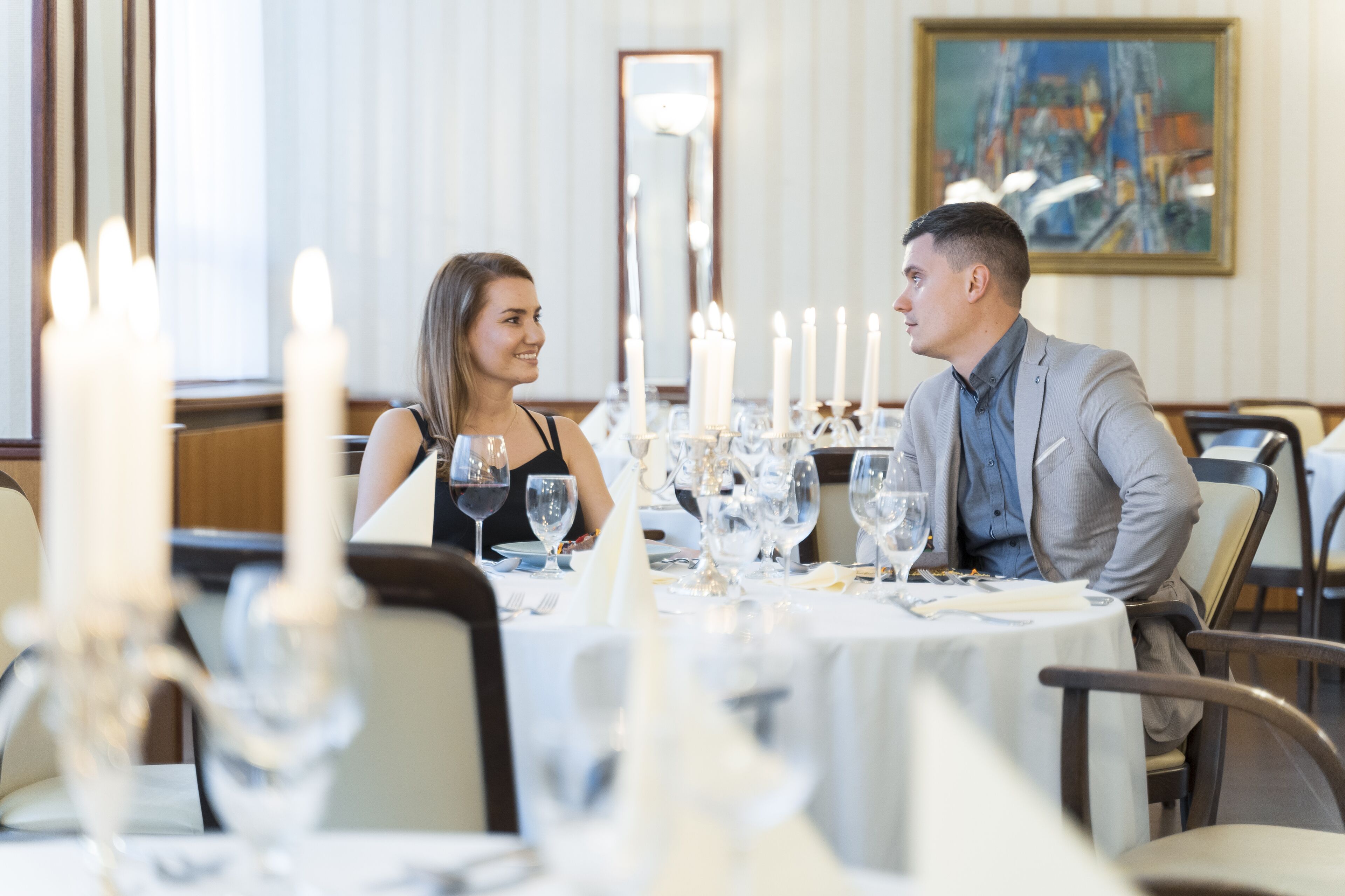 A dining table set with candles, wine glasses, and plates, in a room with a large mirror and a painting on the wall.