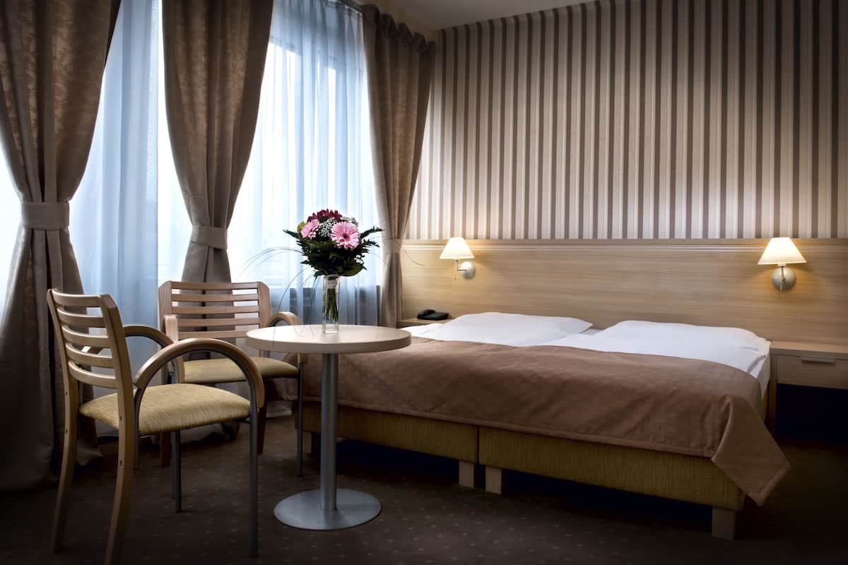 A hotel room with a bed, bedside lamps, a table with a vase of flowers, and a chair.