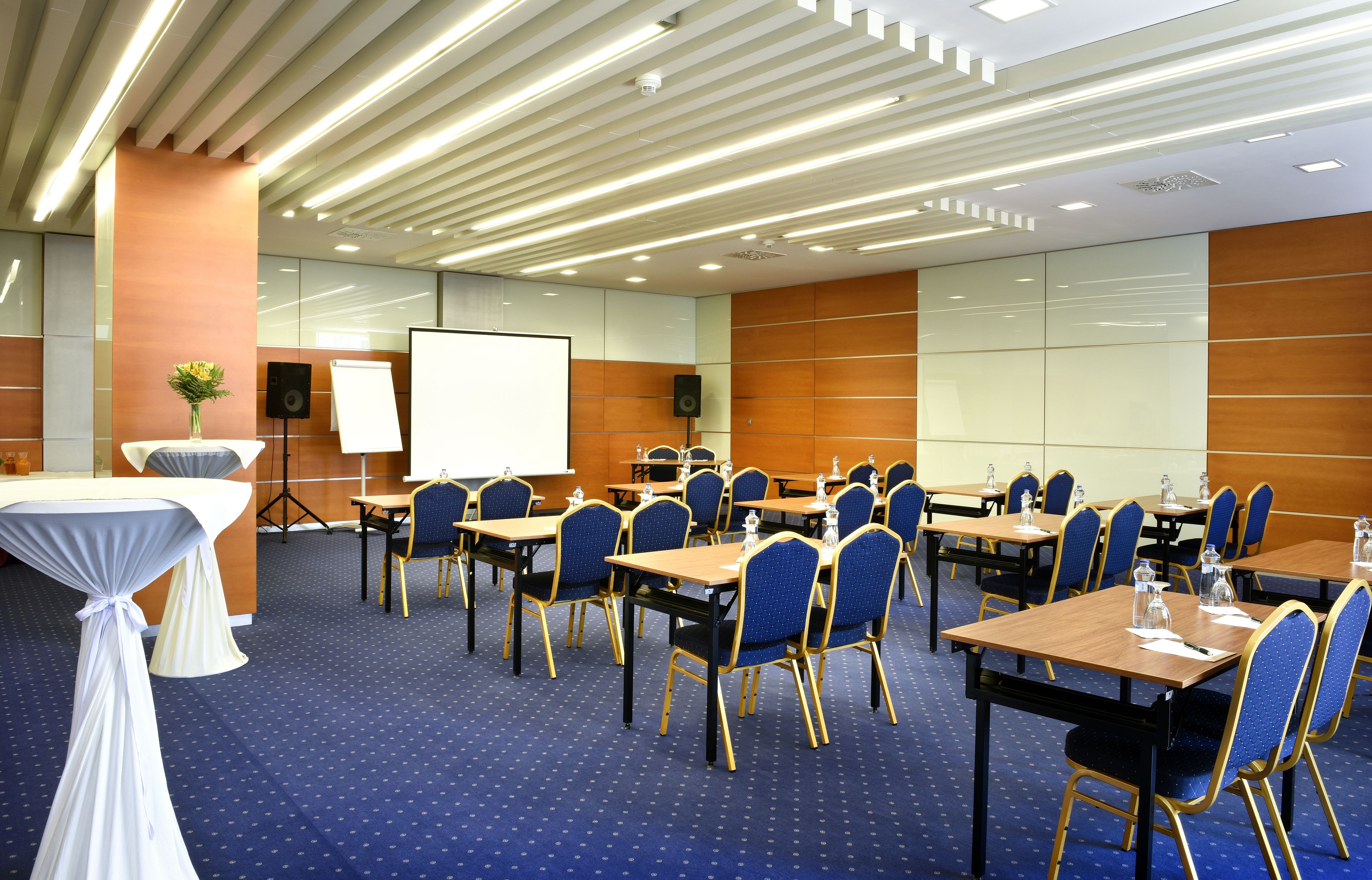 A conference room with tables, chairs, a whiteboard, and a projector screen.