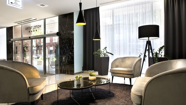 Um hall de hotel moderno com sofás de couro, uma mesa de centro de vidro e uma grande janela com cortinas.