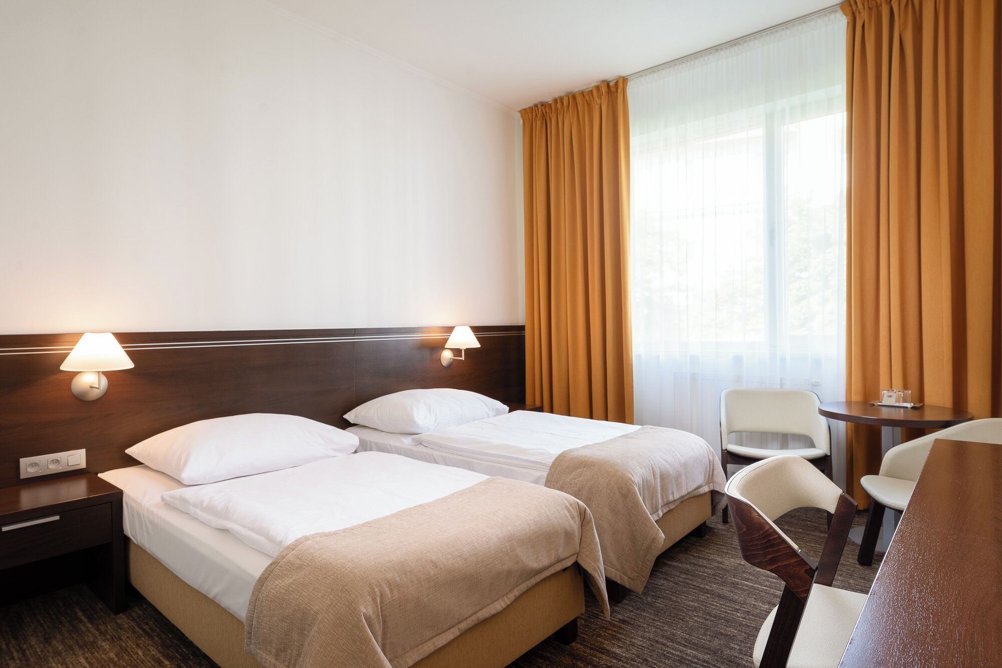 Une chambre d’hôtel avec deux lits, un bureau, une chaise et une fenêtre avec des rideaux.