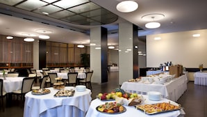 Disposição de buffet com mesas cobertas por toalhas brancas, exibindo uma variedade de alimentos, incluindo frutas, doces e outros pratos.