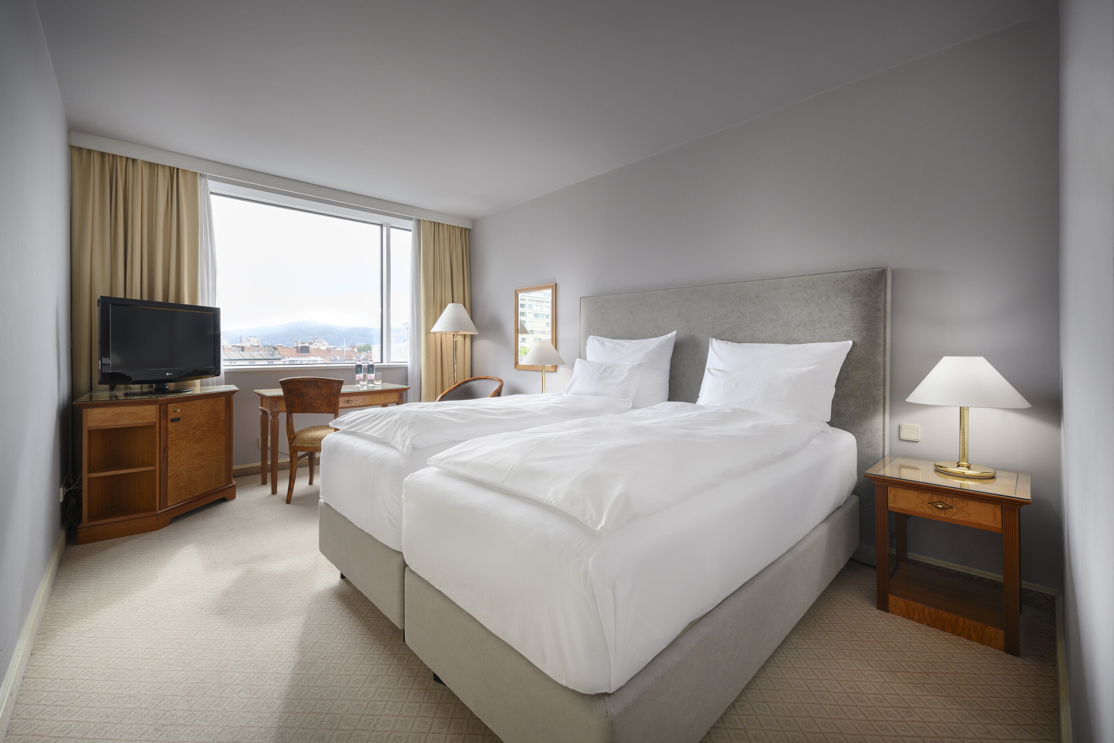 A hotel room with two beds, a desk with a television, and a chair.