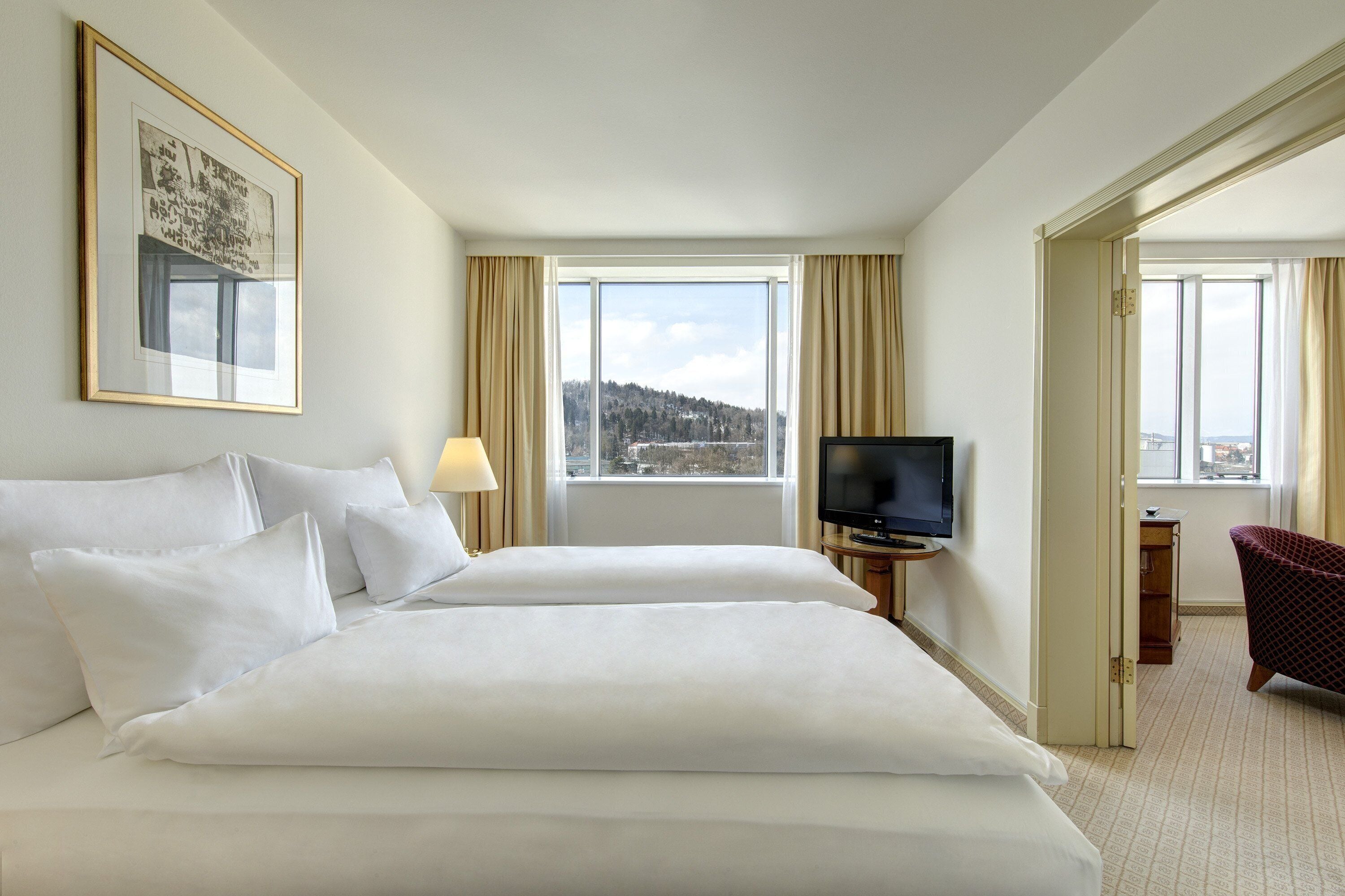 Habitación de hotel con dos camas, un televisor, un cuadro enmarcado en la pared y vista a una ciudad a través de la ventana.