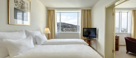 Habitación de hotel con dos camas, un televisor, un cuadro enmarcado en la pared y vista a una ciudad a través de la ventana.