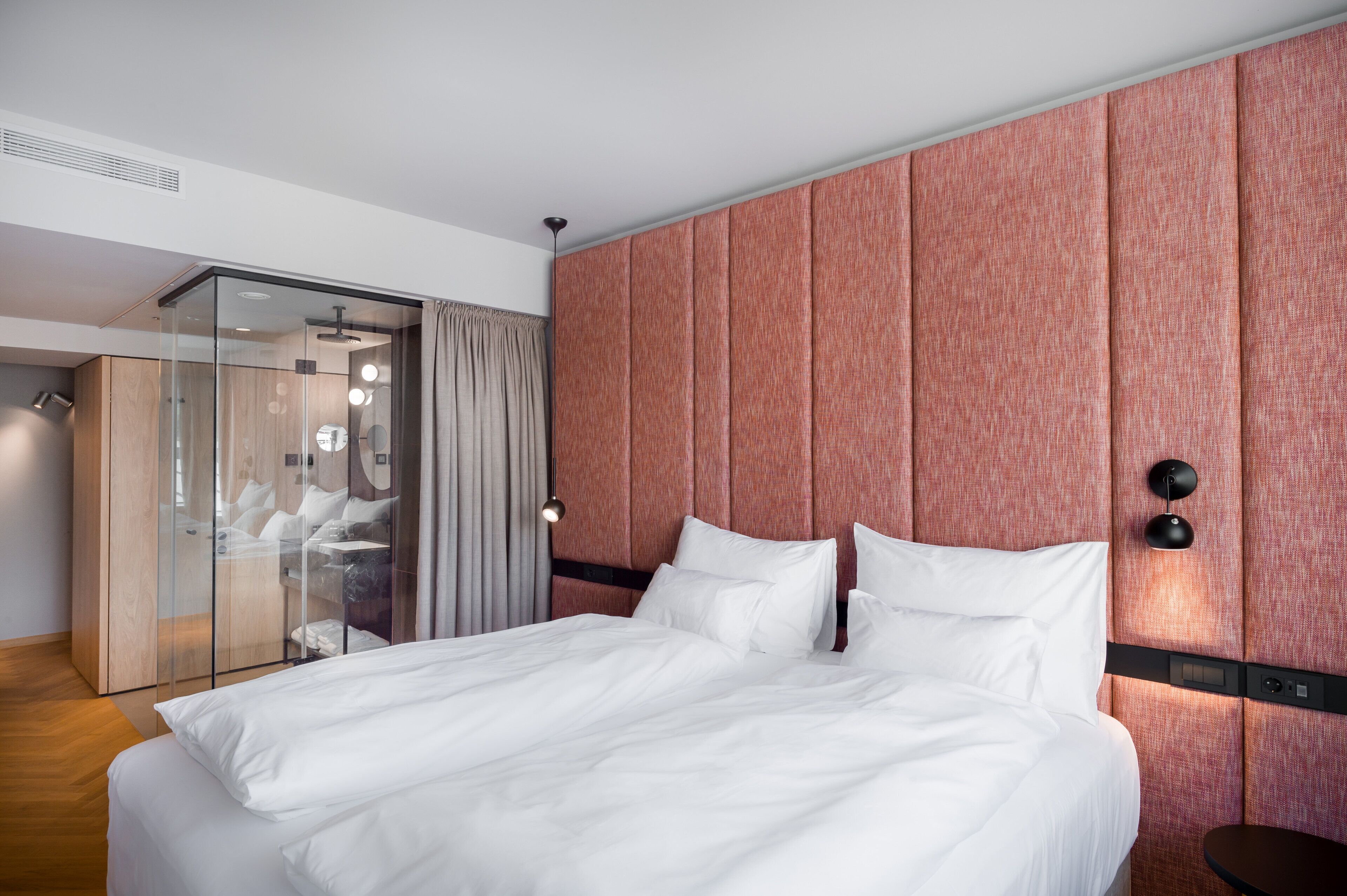 A hotel room with a large bed, a glass shower enclosure, and a wooden wardrobe.