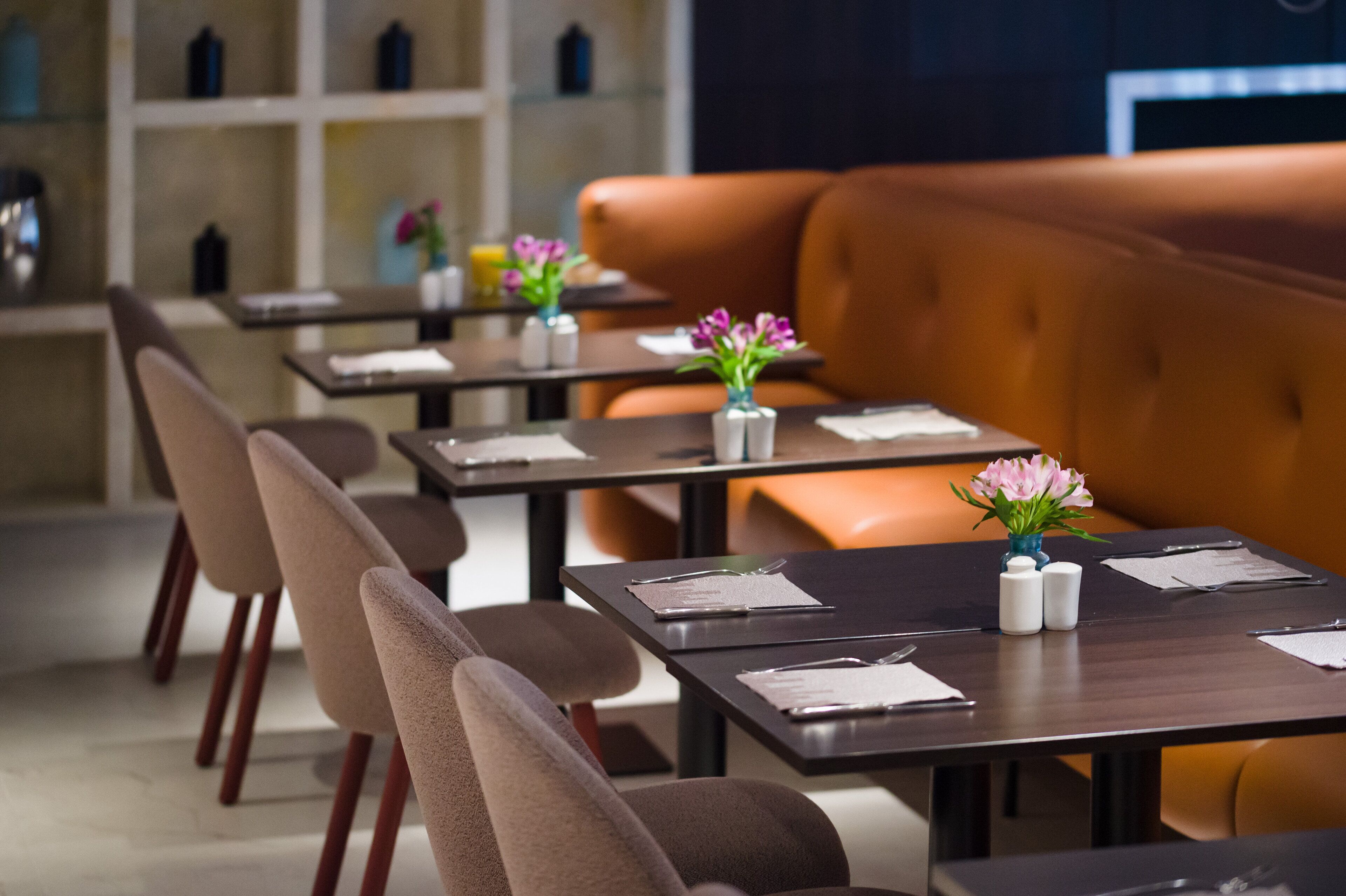 A modern restaurant with multiple tables, each with a vase of flowers, and a large orange sofa.